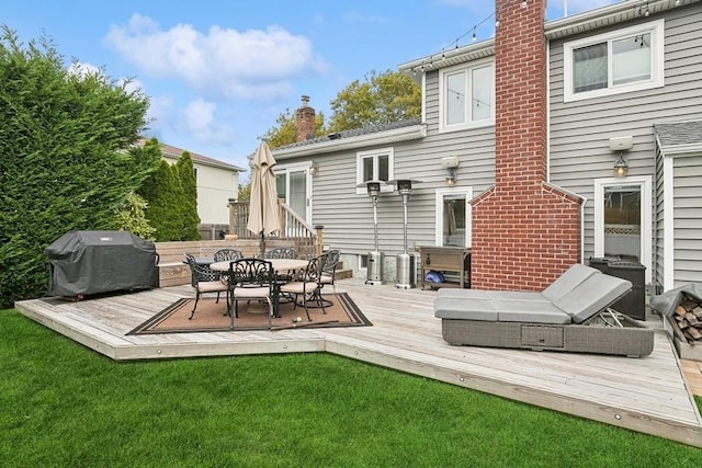 back of property with a deck, outdoor dining area, a yard, and a chimney