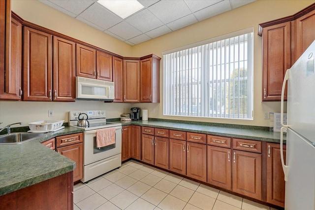 kitchen featuring white appliances, a drop ceiling, dark countertops, brown cabinets, and a sink