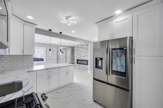 kitchen featuring light stone counters, stainless steel fridge, hanging light fixtures, and white cabinets