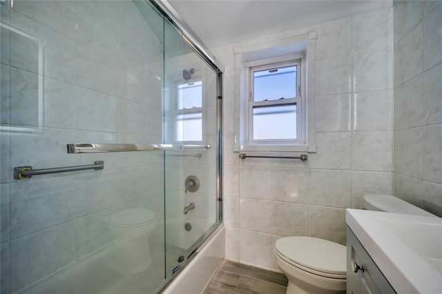 full bathroom featuring hardwood / wood-style flooring, enclosed tub / shower combo, tile walls, vanity, and toilet