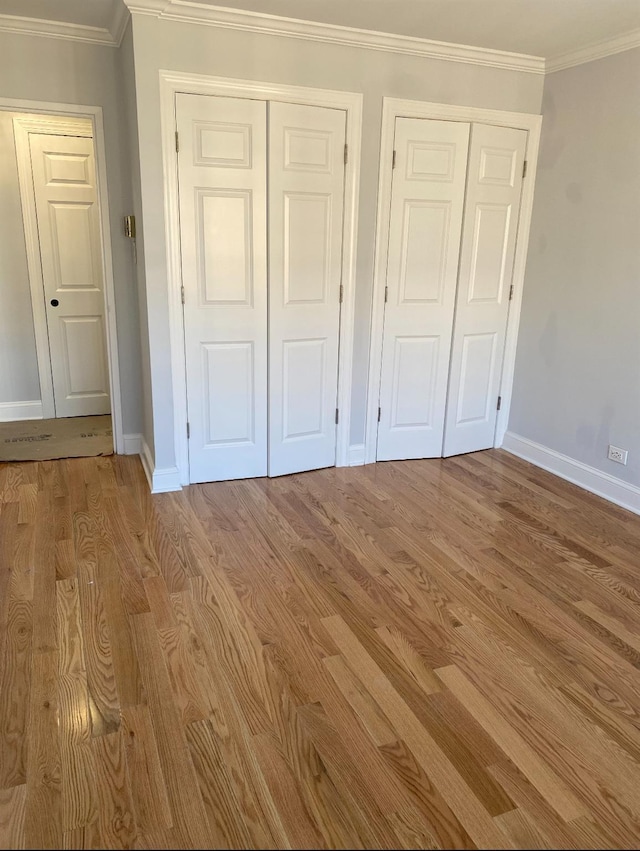 unfurnished bedroom with multiple closets, ornamental molding, and light hardwood / wood-style floors