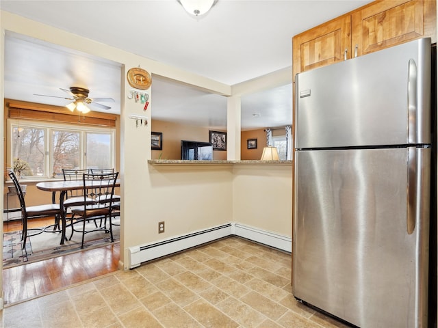 kitchen featuring light stone counters, a baseboard heating unit, stainless steel fridge, and ceiling fan