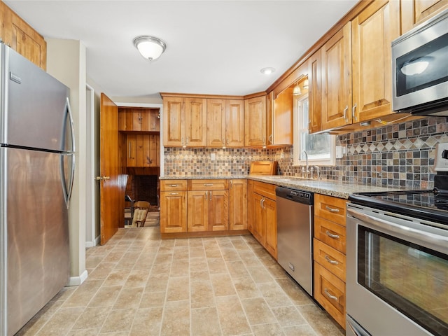 kitchen with stainless steel appliances, sink, backsplash, and light stone counters