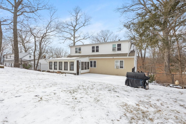 snow covered back of property with a sunroom