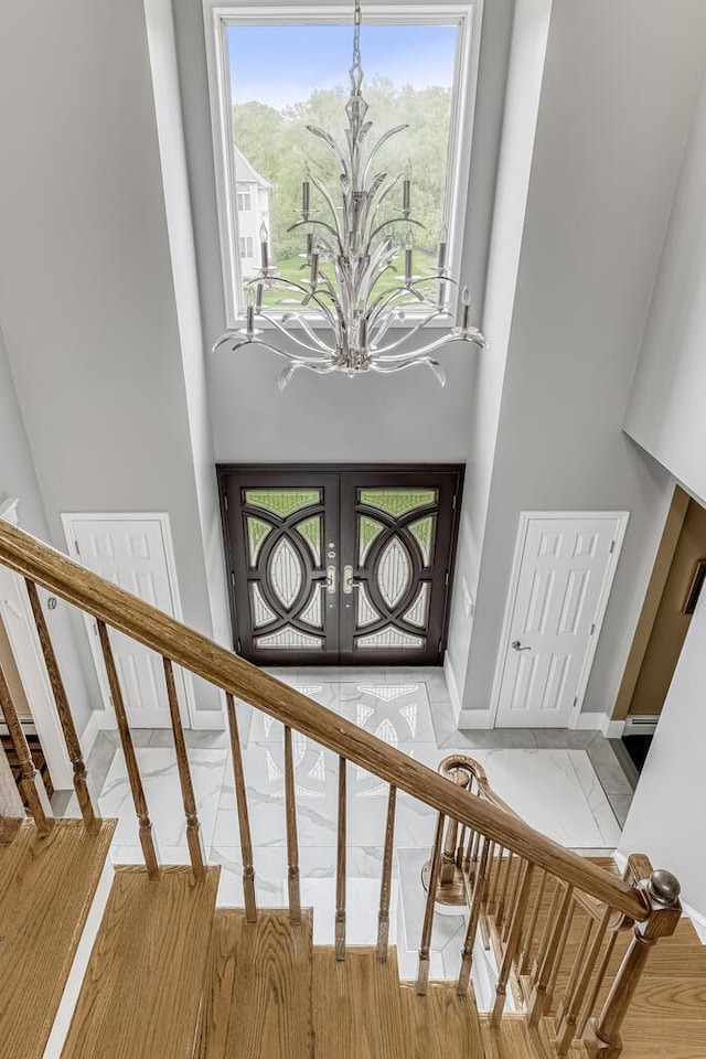 stairs with a chandelier, a towering ceiling, baseboards, marble finish floor, and french doors