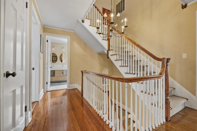 stairway featuring hardwood / wood-style flooring, ornamental molding, and a notable chandelier