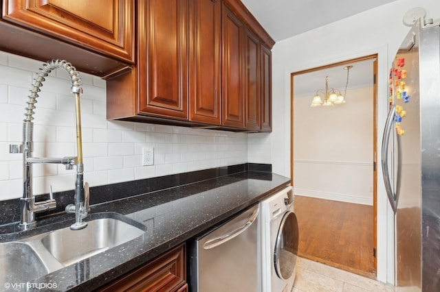 kitchen with sink, tasteful backsplash, dark stone countertops, stainless steel appliances, and washer / clothes dryer