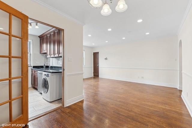 kitchen with sink, crown molding, light hardwood / wood-style flooring, washer / clothes dryer, and decorative backsplash