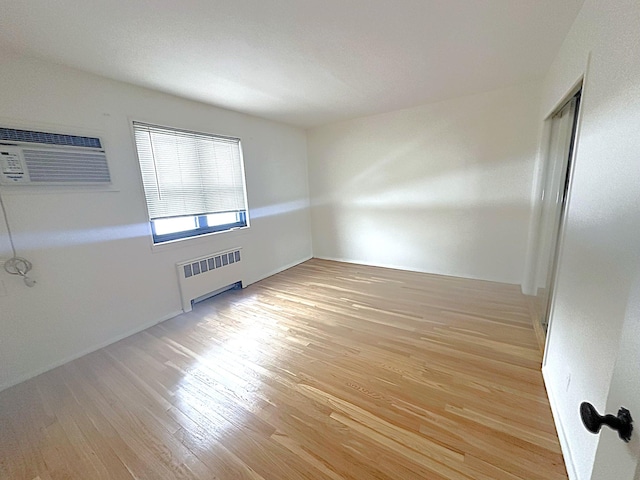 spare room with radiator heating unit, a wall mounted AC, and light wood-type flooring