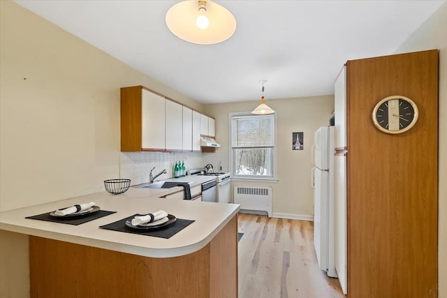 kitchen with decorative light fixtures, radiator, kitchen peninsula, white appliances, and white cabinets