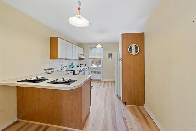 kitchen featuring radiator heating unit, decorative light fixtures, white cabinetry, white refrigerator, and kitchen peninsula