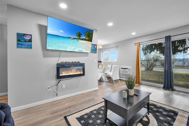 living area featuring baseboards, a glass covered fireplace, wood finished floors, a wall mounted air conditioner, and recessed lighting