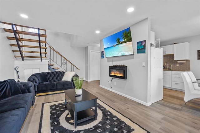 living area featuring recessed lighting, baseboards, stairs, light wood finished floors, and a glass covered fireplace