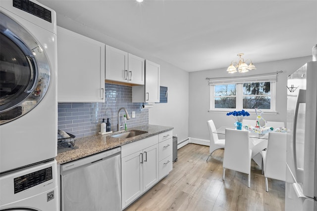 kitchen featuring light wood finished floors, stacked washer / drying machine, refrigerator, stainless steel dishwasher, and a sink