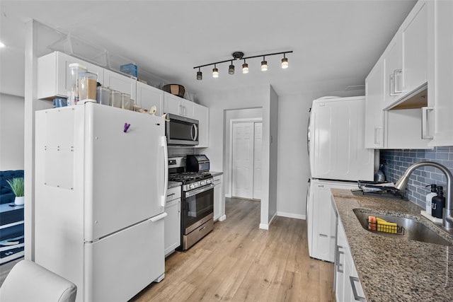 kitchen with light wood-style flooring, stainless steel appliances, a sink, white cabinets, and tasteful backsplash