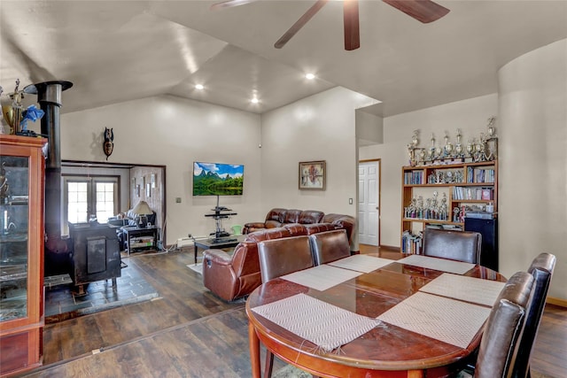 dining space with ceiling fan, dark hardwood / wood-style floors, vaulted ceiling, and a wood stove