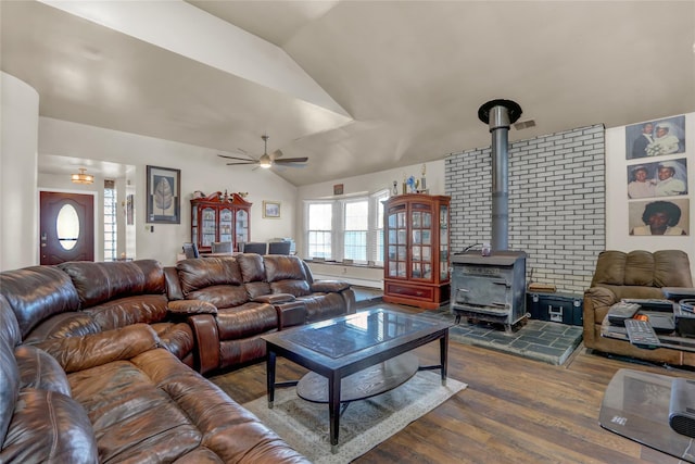 living room with ceiling fan, vaulted ceiling, wood-type flooring, and a wood stove