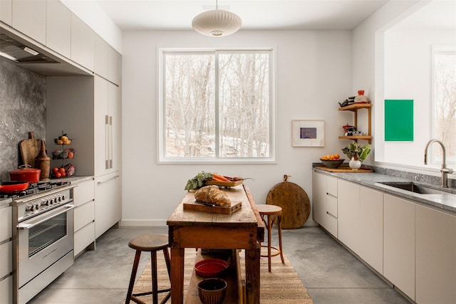 kitchen with finished concrete flooring, stainless steel range, white cabinets, and a sink