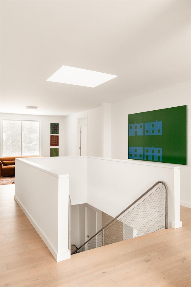 corridor with a skylight, baseboards, an upstairs landing, and wood finished floors