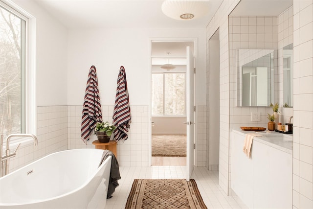 bathroom with a freestanding bath, tile walls, vanity, and tile patterned floors