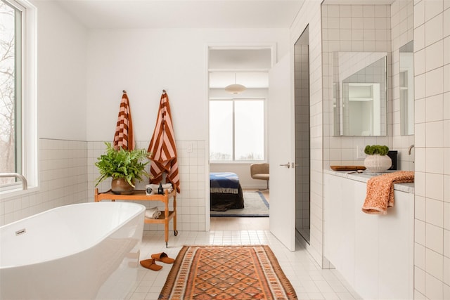 ensuite bathroom with a freestanding tub, ensuite bath, tile patterned flooring, and tile walls