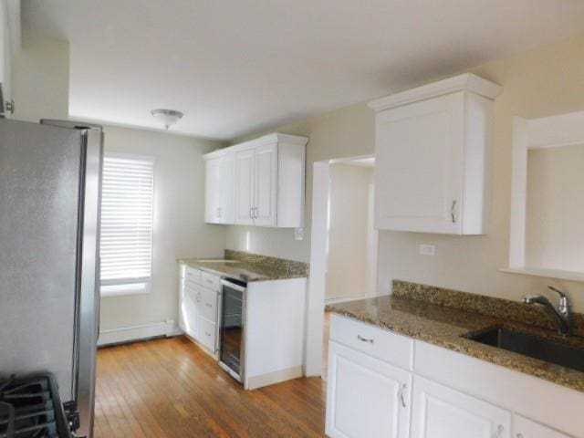 kitchen featuring sink, stainless steel fridge, white cabinetry, wine cooler, and dark stone counters