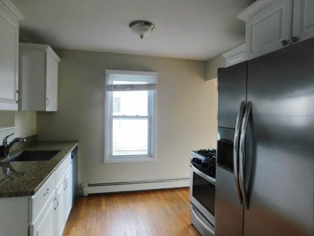 kitchen with a baseboard radiator, sink, dark stone countertops, white cabinets, and stainless steel appliances