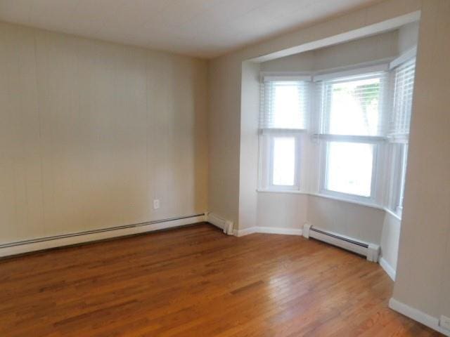 unfurnished room featuring wood-type flooring and a baseboard heating unit