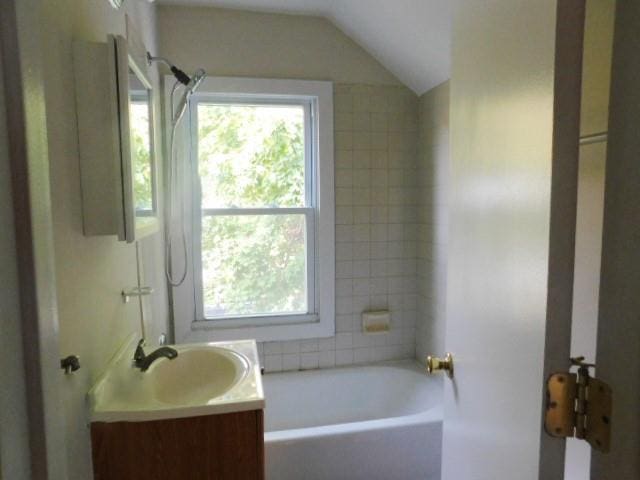 bathroom with a healthy amount of sunlight, vanity, shower / washtub combination, and vaulted ceiling