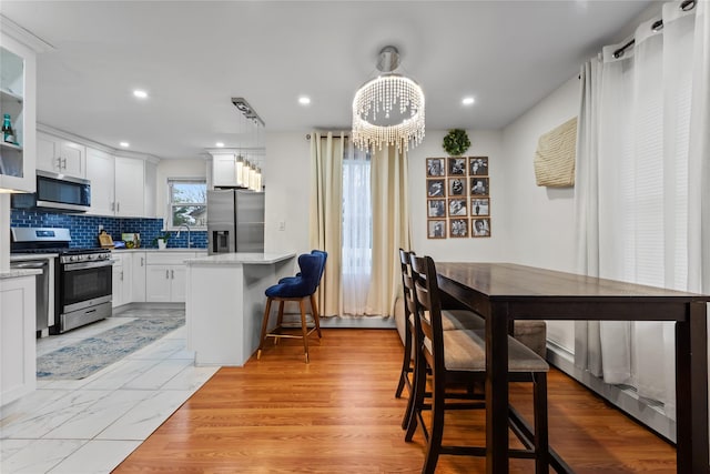 kitchen with appliances with stainless steel finishes, white cabinets, hanging light fixtures, a center island, and light stone countertops