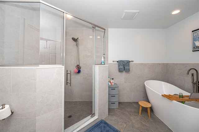 full bath featuring a stall shower, a freestanding tub, and tile walls