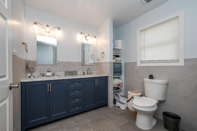 full bathroom with toilet, double vanity, tile walls, and a sink