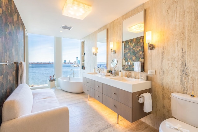 bathroom featuring a bathtub, floor to ceiling windows, a water view, vanity, and toilet