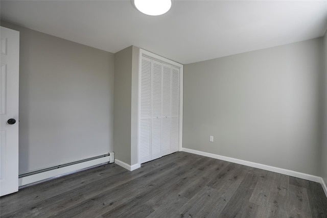 unfurnished bedroom featuring a baseboard heating unit, dark hardwood / wood-style floors, and a closet