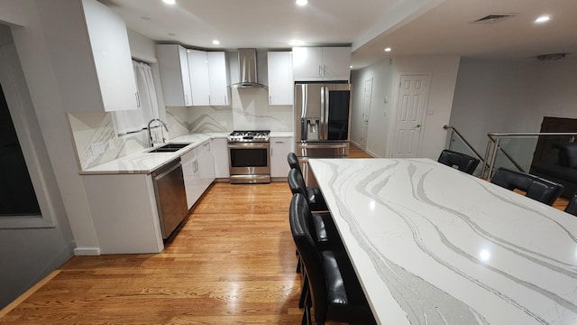 kitchen featuring sink, light hardwood / wood-style flooring, a breakfast bar, stainless steel appliances, and wall chimney exhaust hood