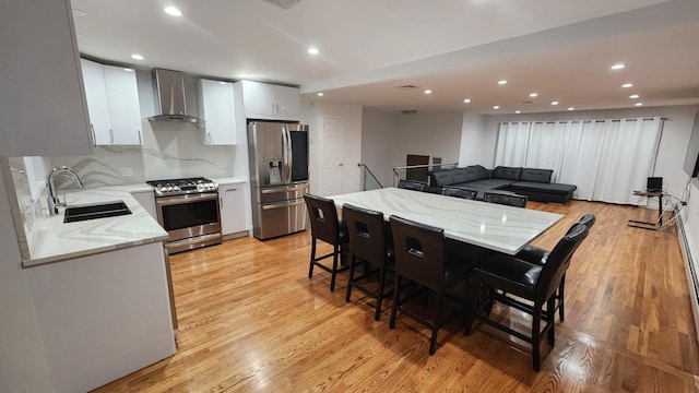 kitchen featuring wall chimney exhaust hood, sink, a breakfast bar area, light hardwood / wood-style flooring, and stainless steel appliances