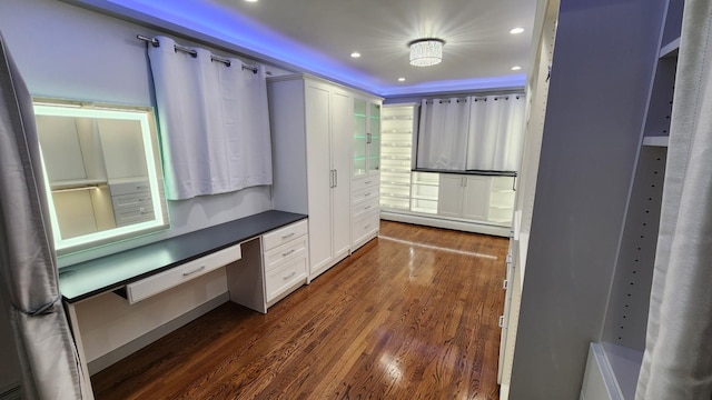 walk in closet featuring dark hardwood / wood-style flooring, built in desk, and a baseboard radiator