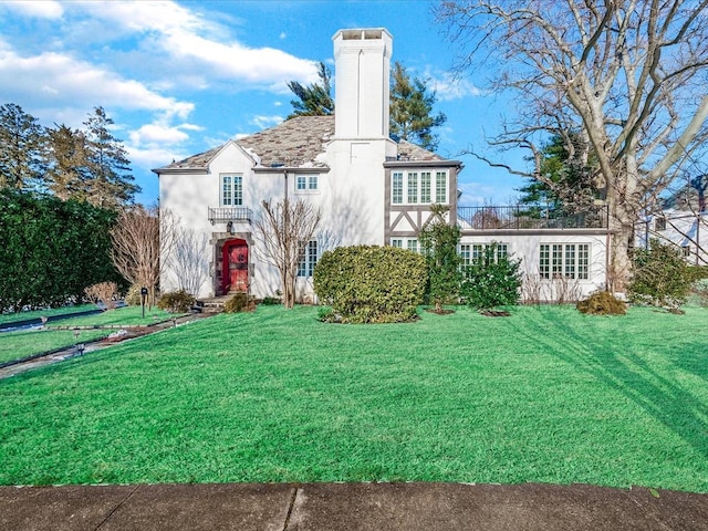 rear view of house featuring a lawn, a chimney, and stucco siding