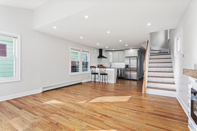 unfurnished living room featuring baseboard heating, sink, and light hardwood / wood-style floors