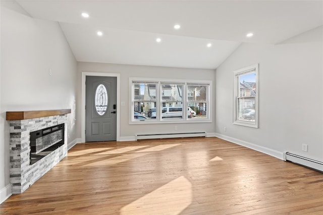 foyer entrance with a stone fireplace, vaulted ceiling, baseboard heating, and light wood-type flooring