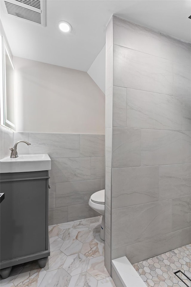 bathroom featuring vanity, a tile shower, tile walls, and toilet