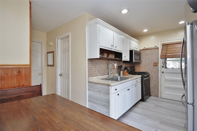 kitchen with a sink, white cabinetry, light wood-style floors, light countertops, and appliances with stainless steel finishes