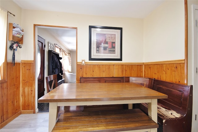 dining space featuring breakfast area, a wainscoted wall, wooden walls, and wood finished floors