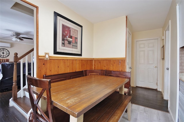 dining room with a wainscoted wall, a ceiling fan, an AC wall unit, wood finished floors, and stairs