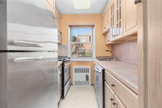 kitchen with light countertops, appliances with stainless steel finishes, glass insert cabinets, light brown cabinets, and a sink