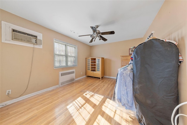 interior space featuring baseboards, a ceiling fan, radiator, a wall unit AC, and light wood-style flooring