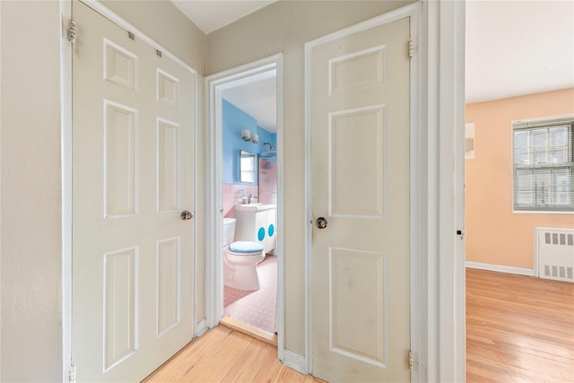 hall with baseboards, a healthy amount of sunlight, radiator heating unit, and light wood-style floors