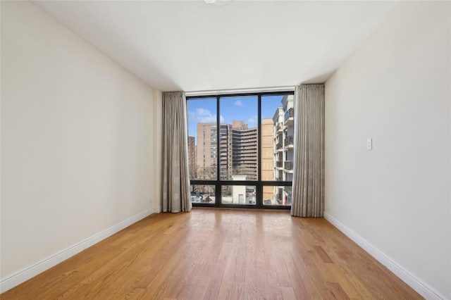 empty room with a view of city, light wood finished floors, a wall of windows, and baseboards