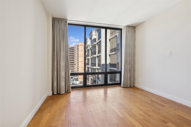 unfurnished room with expansive windows, baseboards, wood finished floors, and a city view