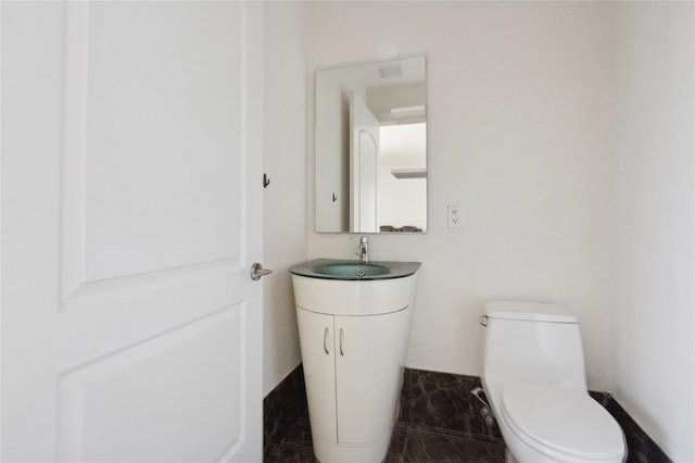 half bath featuring toilet, marble finish floor, and vanity